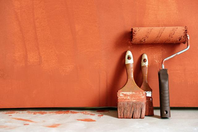 Paintbrush dipped in vibrant orange paint for wall painting and house painting.