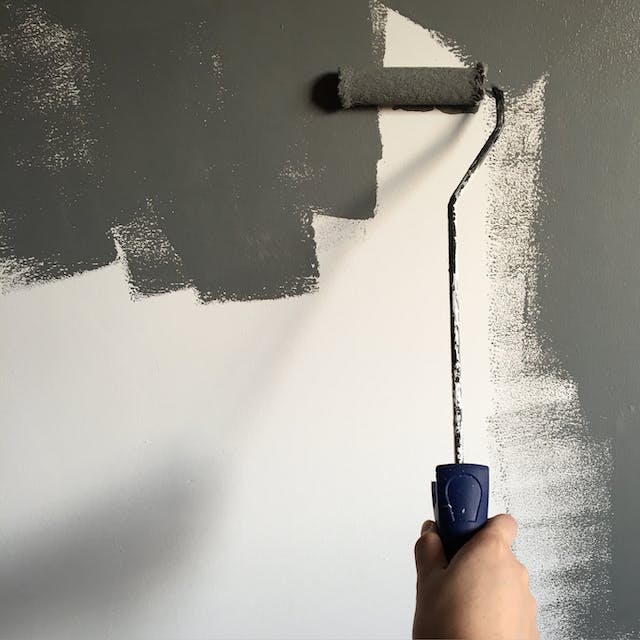 Skilled painter providing painting services, meticulously applying dark grey paint to a wall for a sophisticated and modern look.